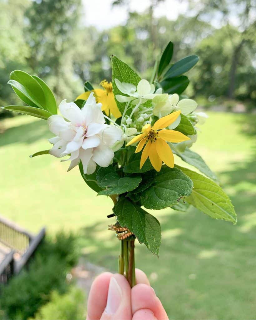 white, yellow, and green mini flower bouquet with grass behind it.