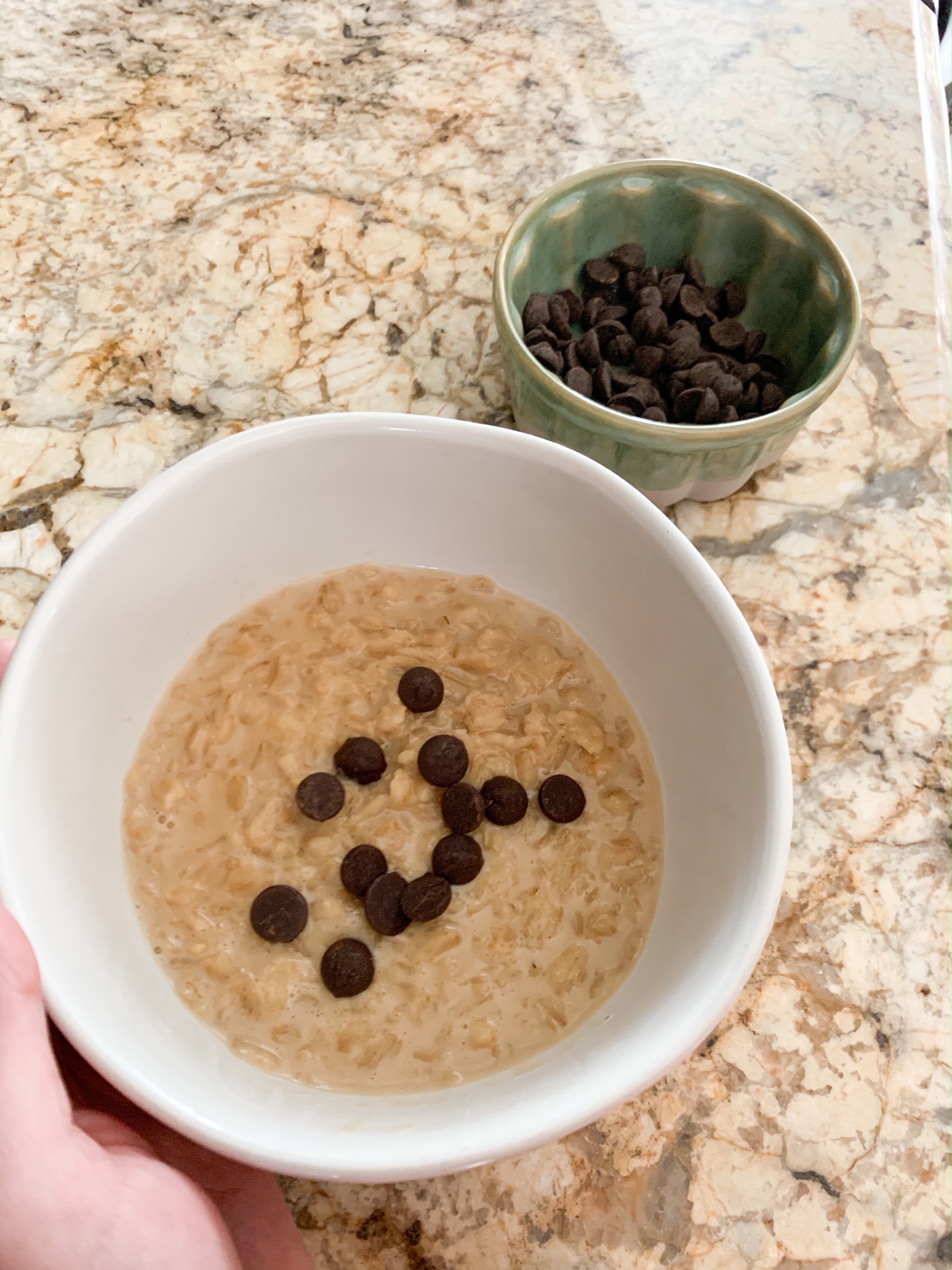 oatmeal with chocolate chips in a white bowl with a small green bowl with chocolate chips on a granite countertop