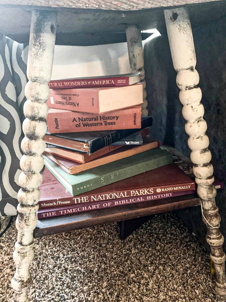 a bunch of old books piled under a side a wood side table
