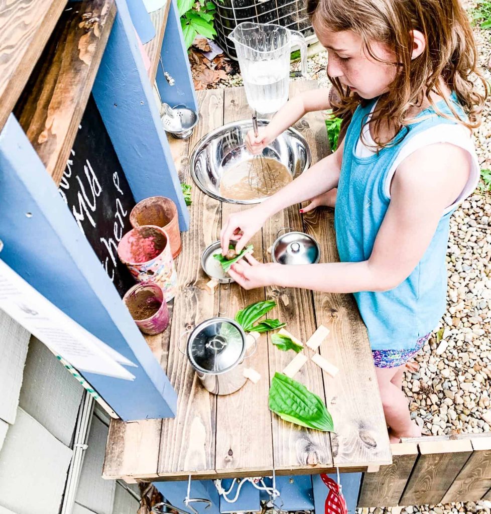 child creating pretend lettuce food on a wooden children's mud kitchen