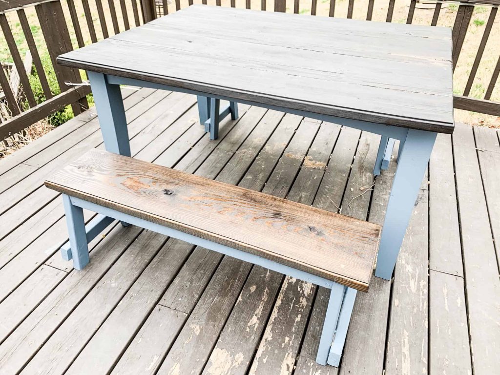 wood outdoor table with blue painted legs on a brown deck
