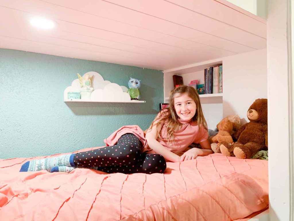 salmon bedding with a cloud shelf and bookcase built in. Little girl sitting.